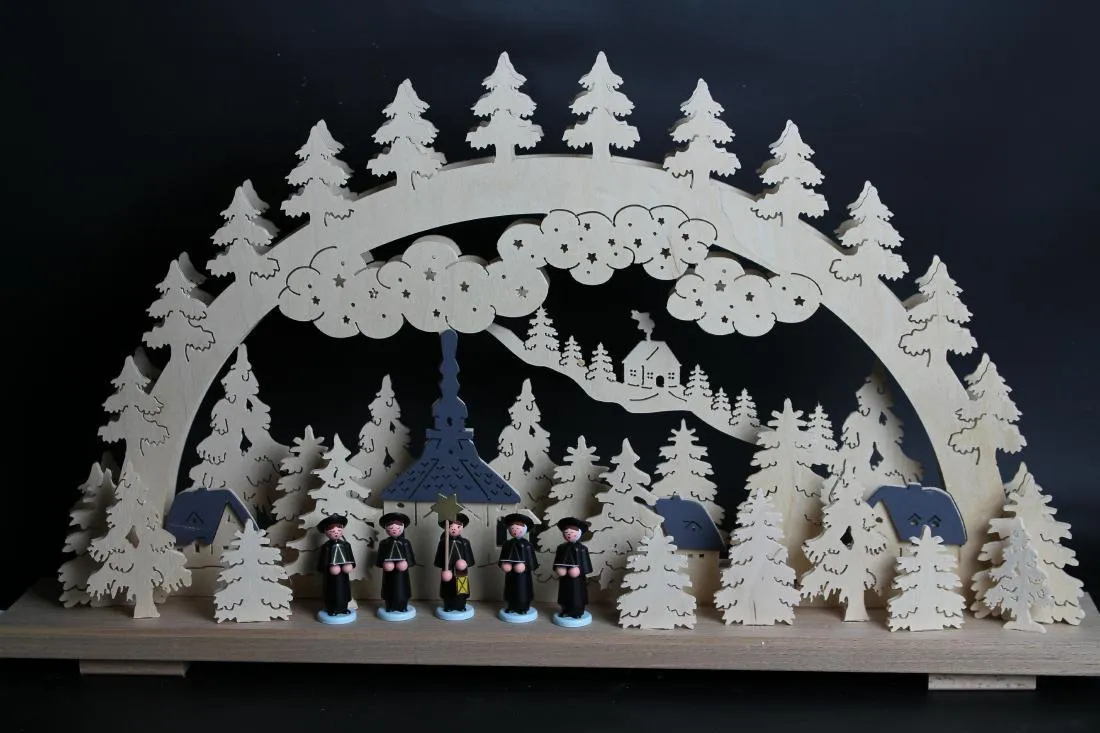 Schwibbogen mit detailreicher Kirche und winterlicher Kurrende, naturfarbenes Holz, beleuchtet von