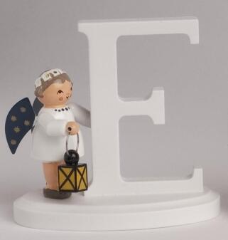 Miniaturfigur Engel aus Holz mit weißem Gewand, blauen Flügeln und Laterne neben Buchstabe E von KWO