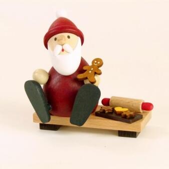 Holzfigur Weihnachtsmann auf roter Bank mit Lebkuchen und Nudelholz, handbemalt von Kunsthandwerk
