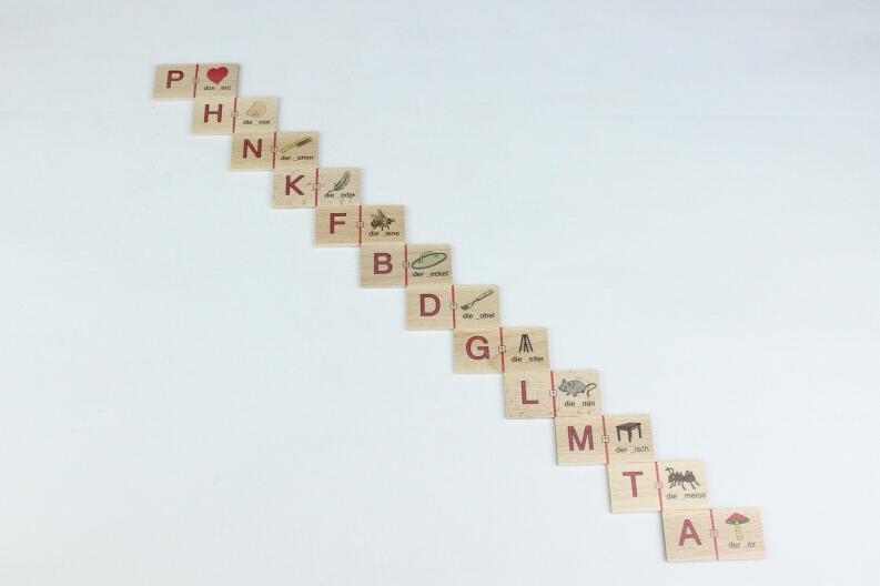 Diagonal angeordnete Holzplättchen mit Buchstaben und kleinen Illustrationen auf hellem Hintergrund